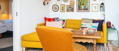 Un salón acogedor con un sofá amarillo mostaza, una mesa de centro de madera y una alfombra a rayas colorida.