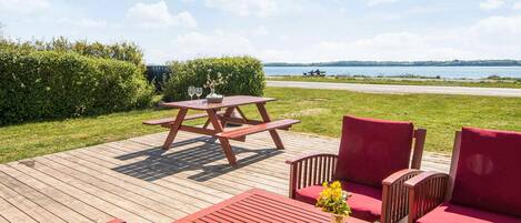 A wooden deck with picnic tables and red chairs, overlooking a body of water.