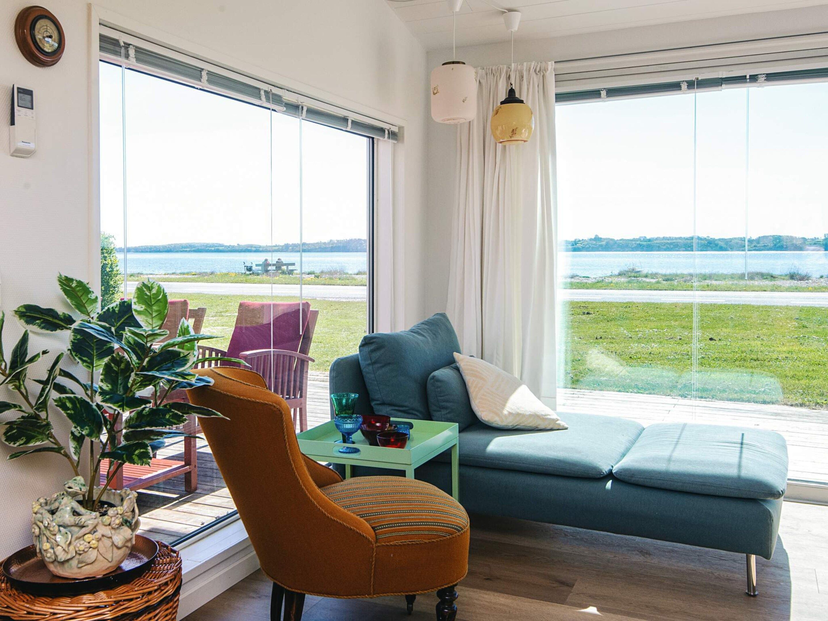 A living room with a view of a lake, a sofa, a chair, and a table with decorative items.
