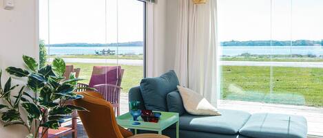 A living room with a view of a lake, a sofa, a chair, and a table with decorative items.