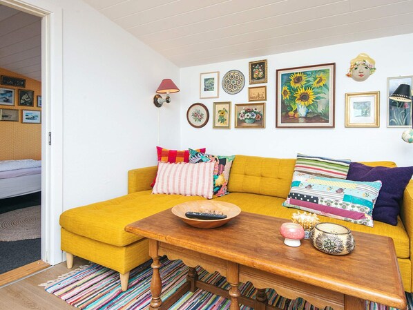 A cozy living room with a mustard-colored sofa, a wooden coffee table, and a variety of colorful pillows.