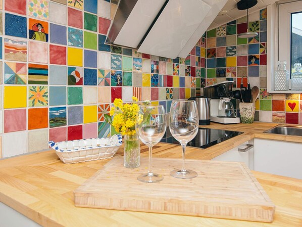 A kitchen with colorful tiles, a wooden countertop, a cutting board, a vase with flowers, and two wine glasses. - 4 Person Holiday Home in Aabenraa (Aabenraa)
