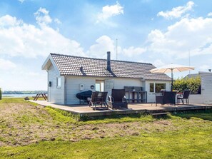 Einbungalow mit Ziegeldach, einer Terrasse und Gartenmöbeln sowie einem Grill.