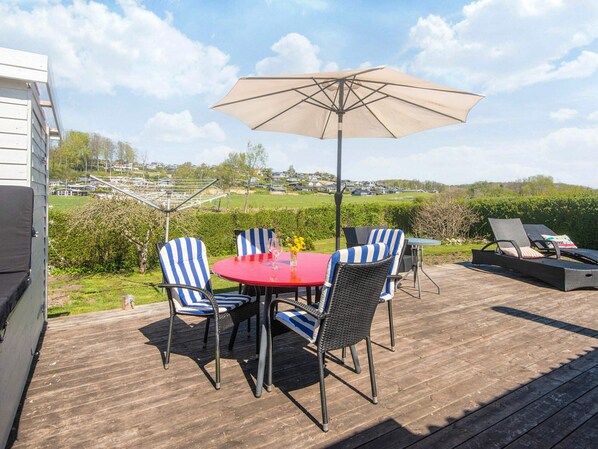 An outdoor patio with a table and chairs, a sun umbrella, and a lounge chair. - 4 Person Holiday Home in Aabenraa (Aabenraa)