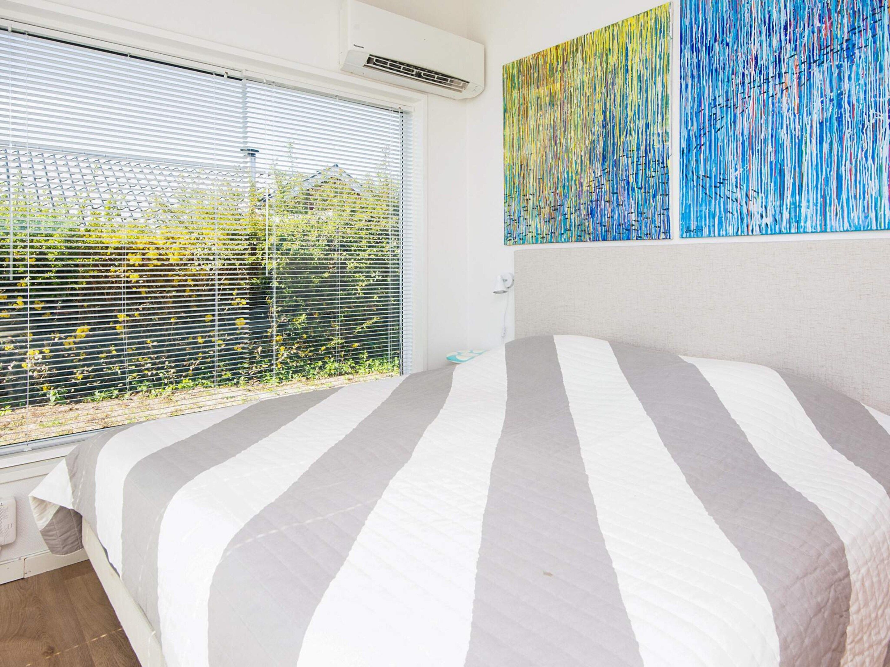 A bedroom with a bed, a window with blinds, and a wall with a painting.