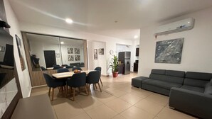 Una sala de estar moderna con un sofá gris, una mesa de comedor con sillas y una cocina al fondo.