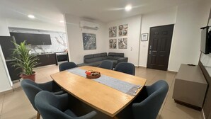 Un comedor con una mesa de madera, sillas azules, una planta en maceta y una cocina al fondo.