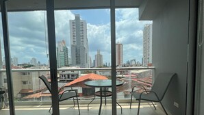 Un balcón con puerta de vidrio, una mesa redonda con sillas y un paraguas rojo.