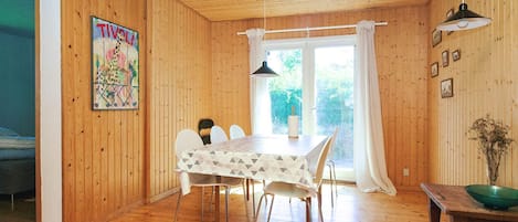 Ein Holzinterieur mit einem Esstisch, Stühlen, einem Gemälde und einem Fenster mit Vorhängen.
