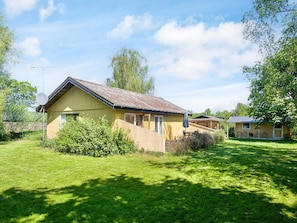 A single-story wooden house with a sloped roof, a satellite dish, and a small patio area with a table and chairs. - 6 Person Holiday Home in Hojby (Hojby)
