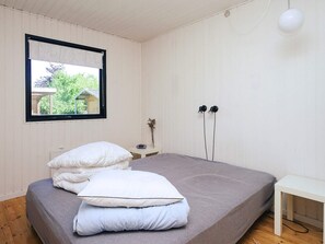 A bedroom with a bed, a bedside table, a window with a view of greenery, and a wall-mounted lamp. - 6 Person Holiday Home in Hojby (Hojby)