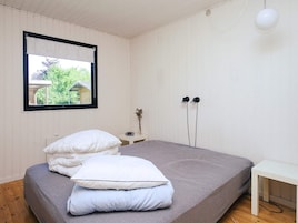 Un dormitorio con cama, mesita de noche, ventana con vista a zonas verdes y lámpara de pared.