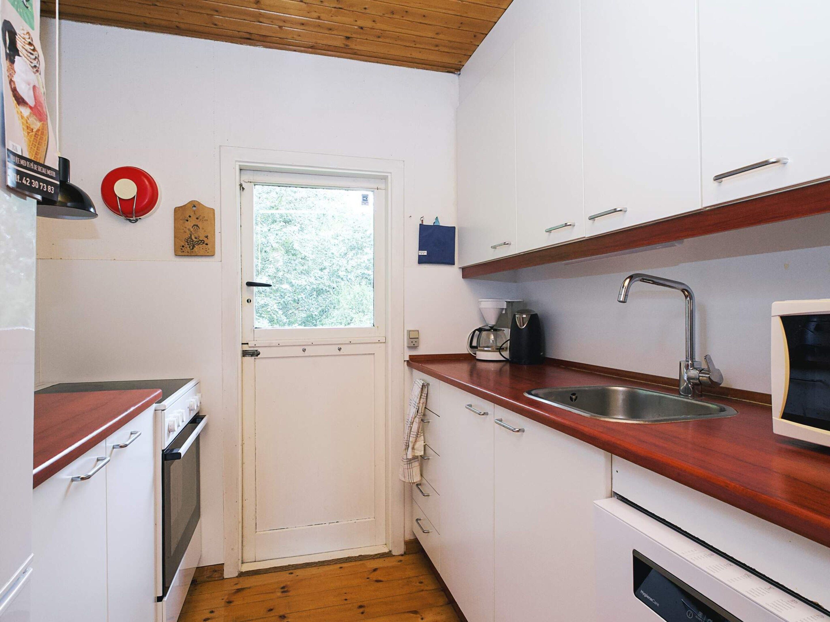 Ett kompakt kök med vita skåp, en bänkskiva i trä, en diskho i rostfritt stål och en kaffebryggare.