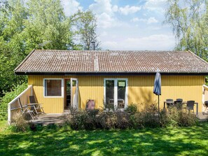Ein gelbes Gebäude mit einem Ziegeldach, einer überdachten Veranda mit Stühlen und einem kleinen Garten.