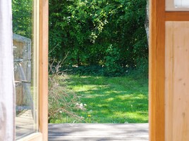 Una terraza de madera que conduce a una zona con césped y follaje denso al fondo.