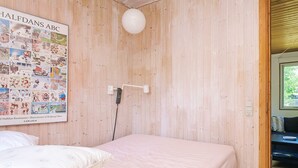 A room with a wooden wall, a bed with white bedding, a poster of Halfdans ABC, and a hanging light fixture. - 6 Person Holiday Home in Hojby (Hojby)