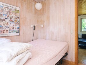 A room with a wooden wall, a bed with white bedding, a poster of Halfdans ABC, and a hanging light fixture. - 6 Person Holiday Home in Hojby (Hojby)