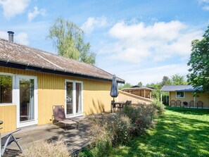 A wooden house with a deck, a sliding glass door, and a patio with a table and chairs. - 6 Person Holiday Home in Hojby (Hojby)