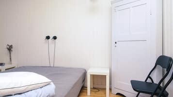 Um quarto com cama, uma cadeira, uma escrivaninha e uma porta.