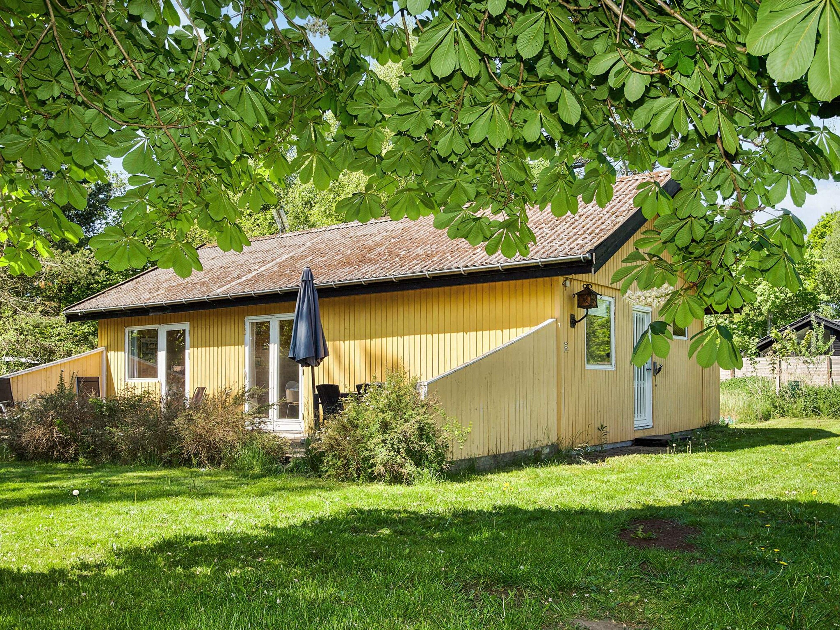 A single-story wooden house with a sloped roof, a front porch, and a small garden area.