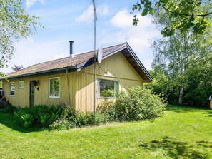 Ein eingeschossiges Holzhaus mit einem geneigten Dach, einem Schornstein und einer Satellitenschüssel.