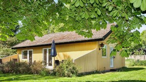 A yellow wooden house with a brown roof, a small porch, and a black umbrella. - 6 Person Holiday Home in Hojby (Hojby)