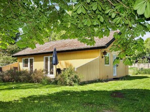 A yellow wooden house with a brown roof, a small porch, and a black umbrella. - 6 Person Holiday Home in Hojby (Hojby)