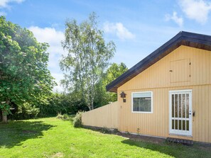A single-story wooden building with a gabled roof, a white-framed window, and a white door with a metal grill. - 6 Person Holiday Home in Hojby (Hojby)
