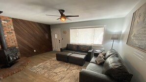 A living room with a fireplace, leather sofas, a ceiling fan, and a large window with blinds. - SilverKing Family Retreat - Dog Friendly! (Show Low)