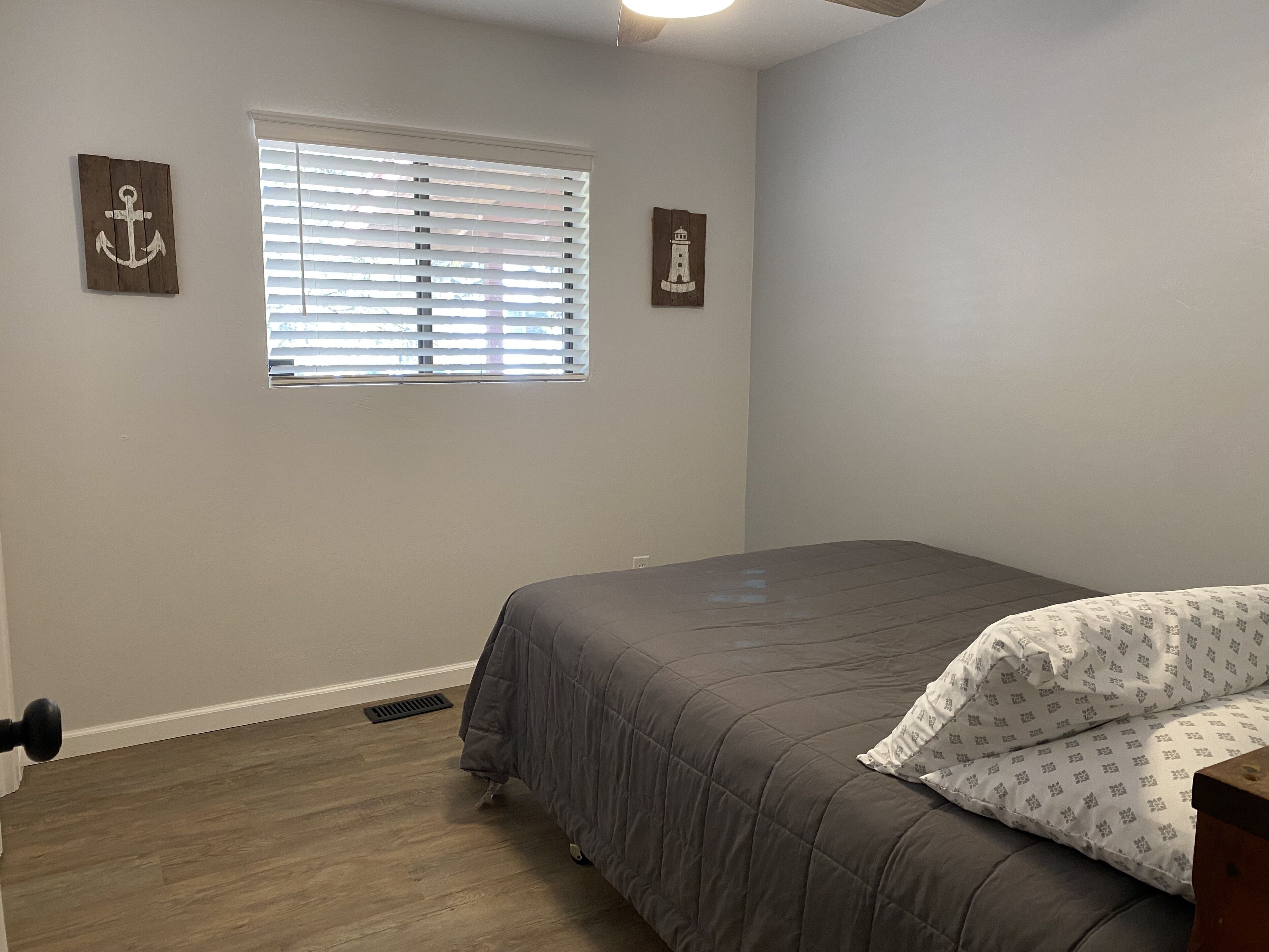 A bedroom with a bed, a window with blinds, and two wall-mounted pictures.