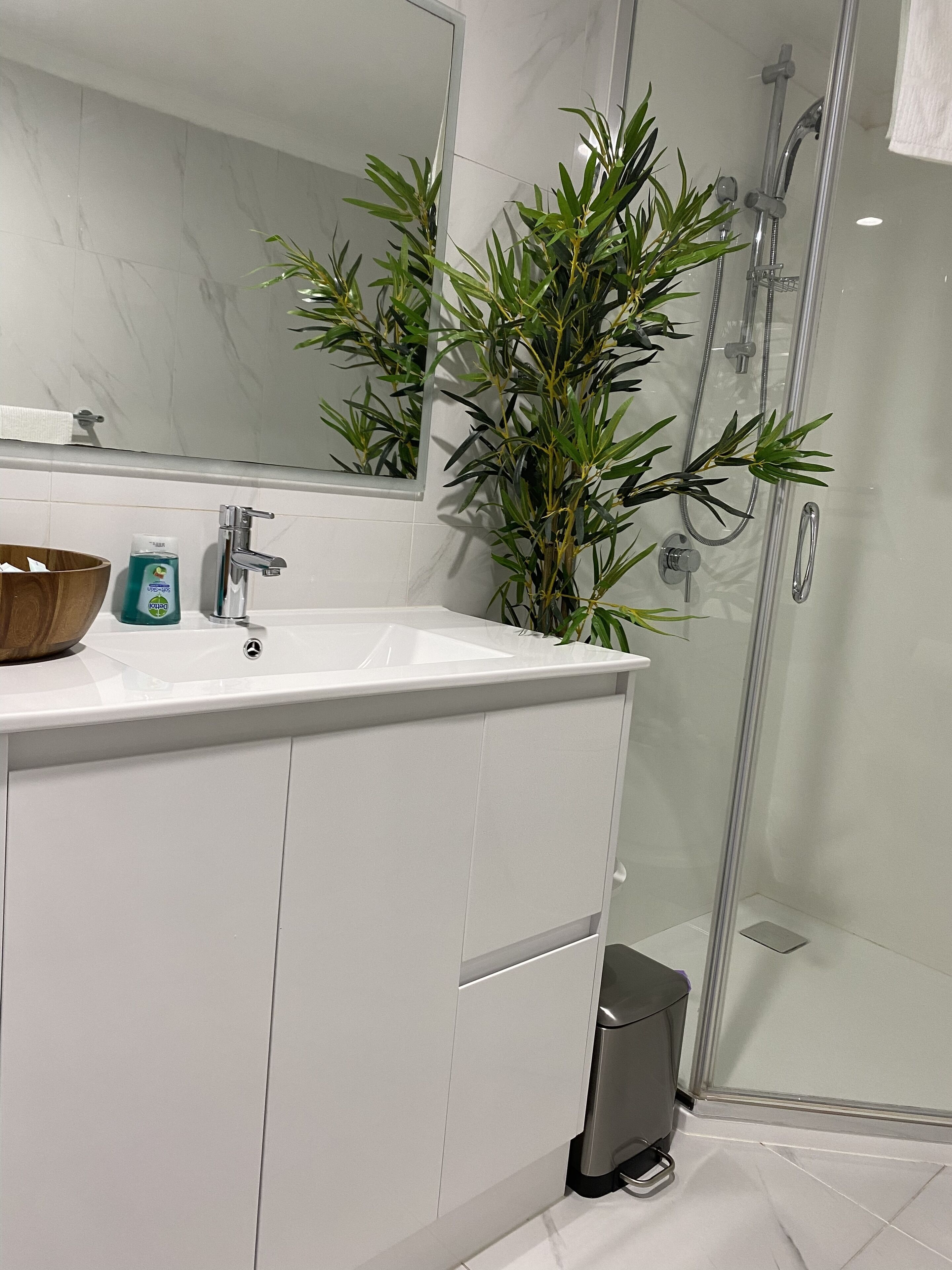 A modern bathroom with a white sink, a mirror, a shower, and a potted plant.
