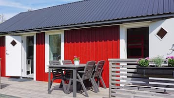 A red and white building with a metal roof, a wooden deck, and a table with chairs.