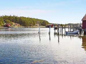 Et roligt sø med en moler, en lille båd og røde bygninger i baggrunden.