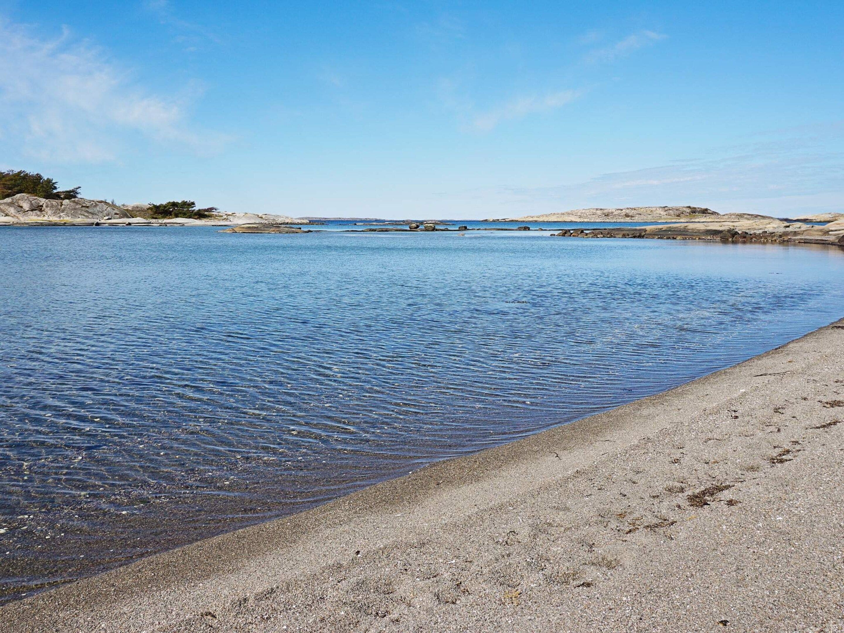 A calm body of water with a sandy beach and rocky outcrops in the distance.