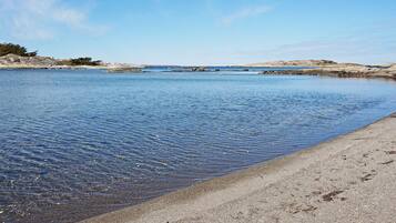 A calm body of water with a sandy beach and rocky outcrops in the distance.