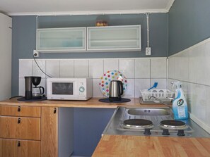 A compact kitchen with a microwave, coffee maker, kettle, and a sink with a dish rack.