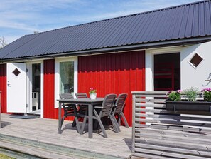 A building with a red exterior, a dark roof, and a wooden deck with a table and chairs. - 4 Person Holiday Home in Stromstad (Stromstad)