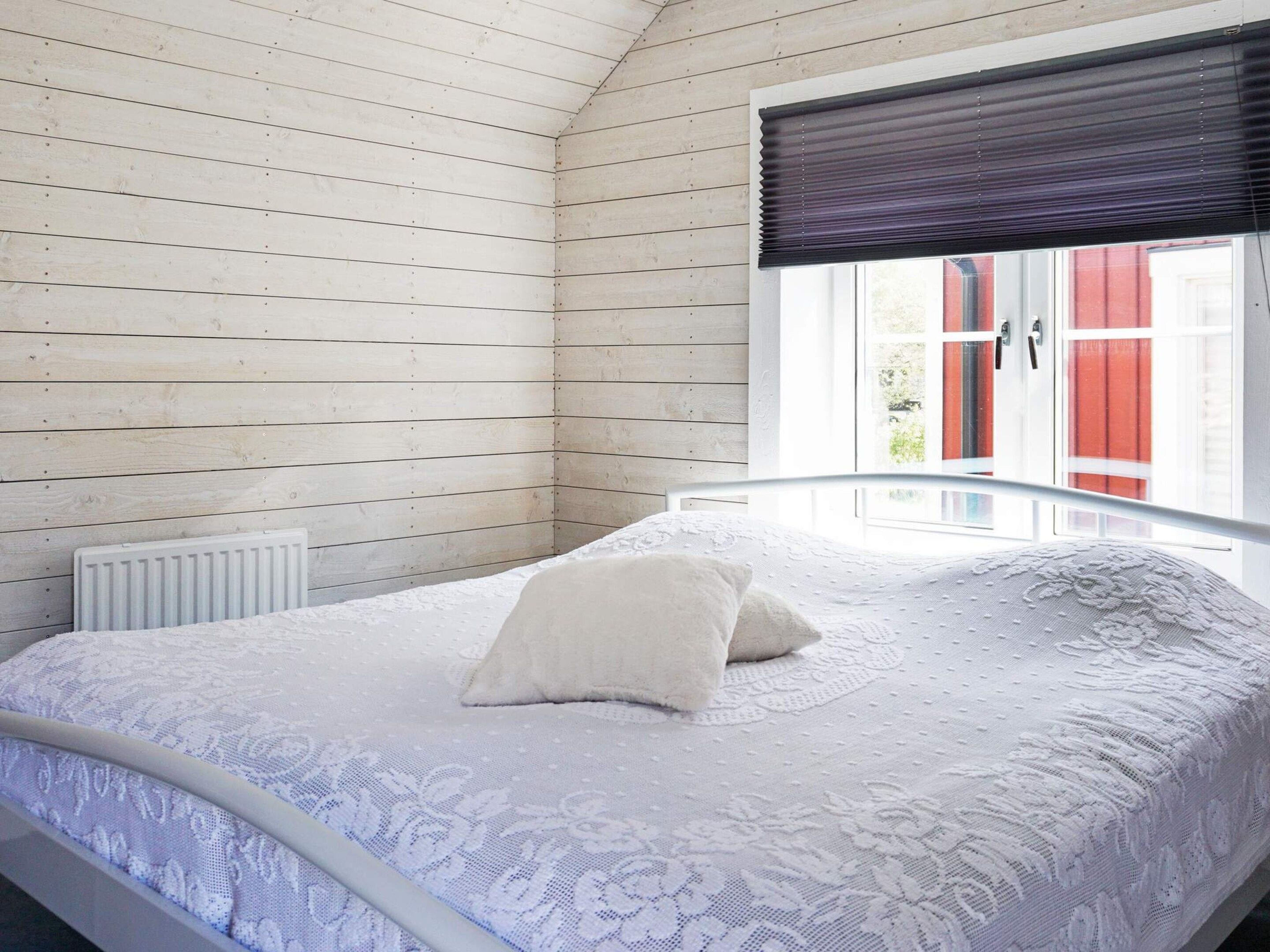 A bedroom with a bed, a radiator, and a window with a view of red buildings.