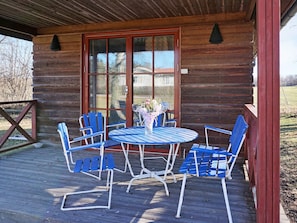Eine Holzhütte mit einer Veranda, einem runden Tisch mit blauen Stühlen und einem großen Fenster.
