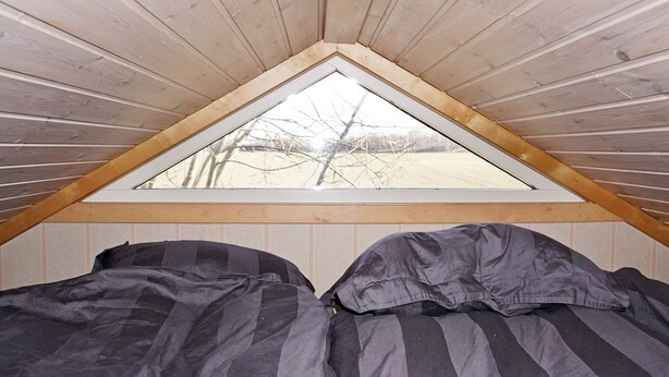 Ein kleines Schlafzimmer im Dachgeschoss mit schrägen Wänden und einem dreieckigen Fenster.