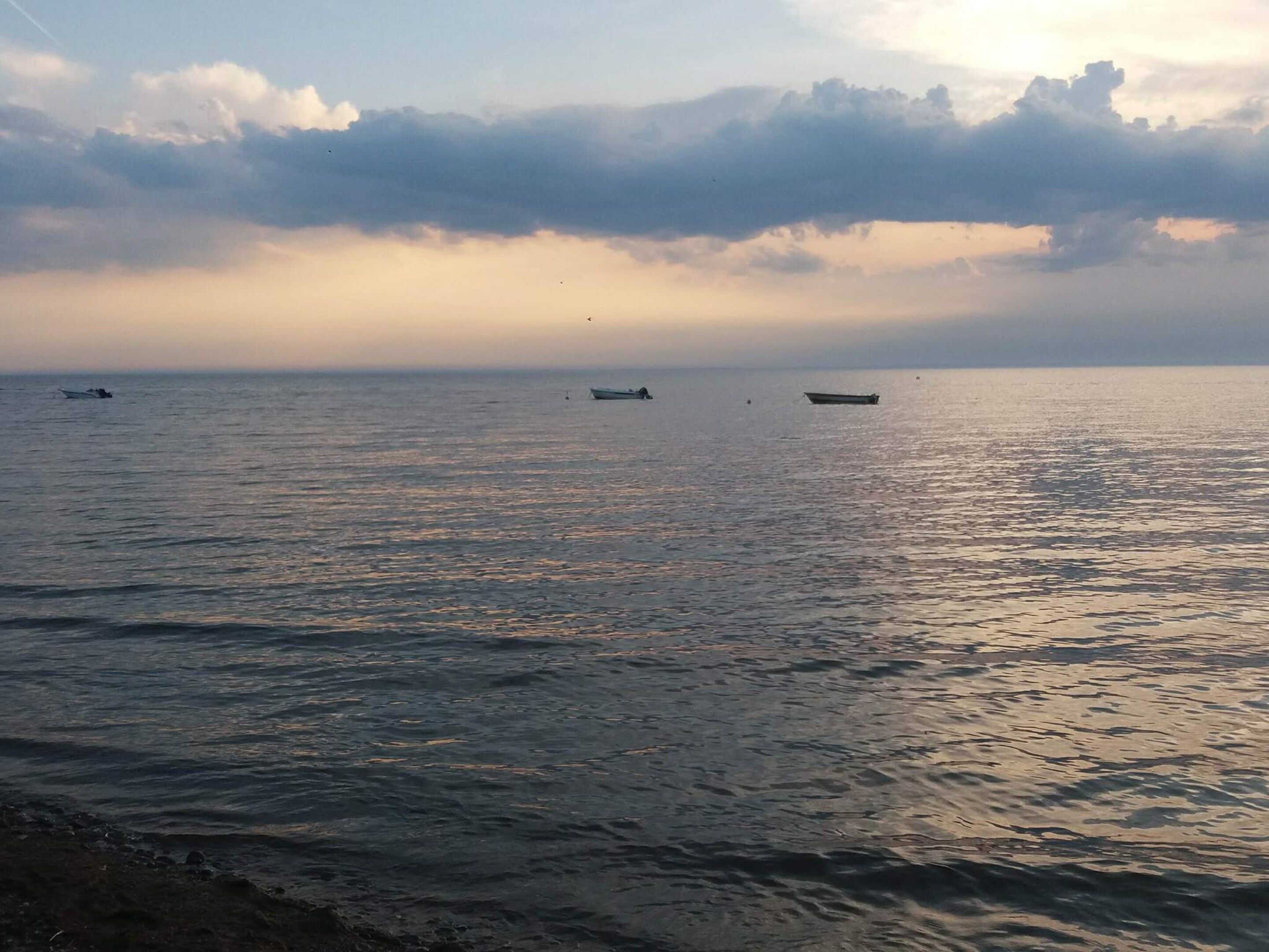 A calm sea with boats and a cloudy sky.