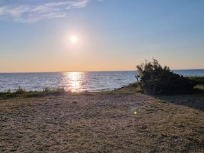 A beach with the sun setting over the water, a grassy area, and some bushes. - 4 Person Holiday Home in Morbylanga (Morbylanga)