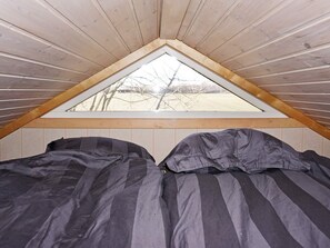 Un pequeño dormitorio en el ático con techo inclinado y ventana triangular.