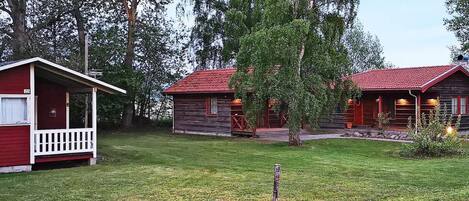 Uma fileira de cabanas com telhados vermelhos e paredes de madeira, cercada por um gramado e árvores.
