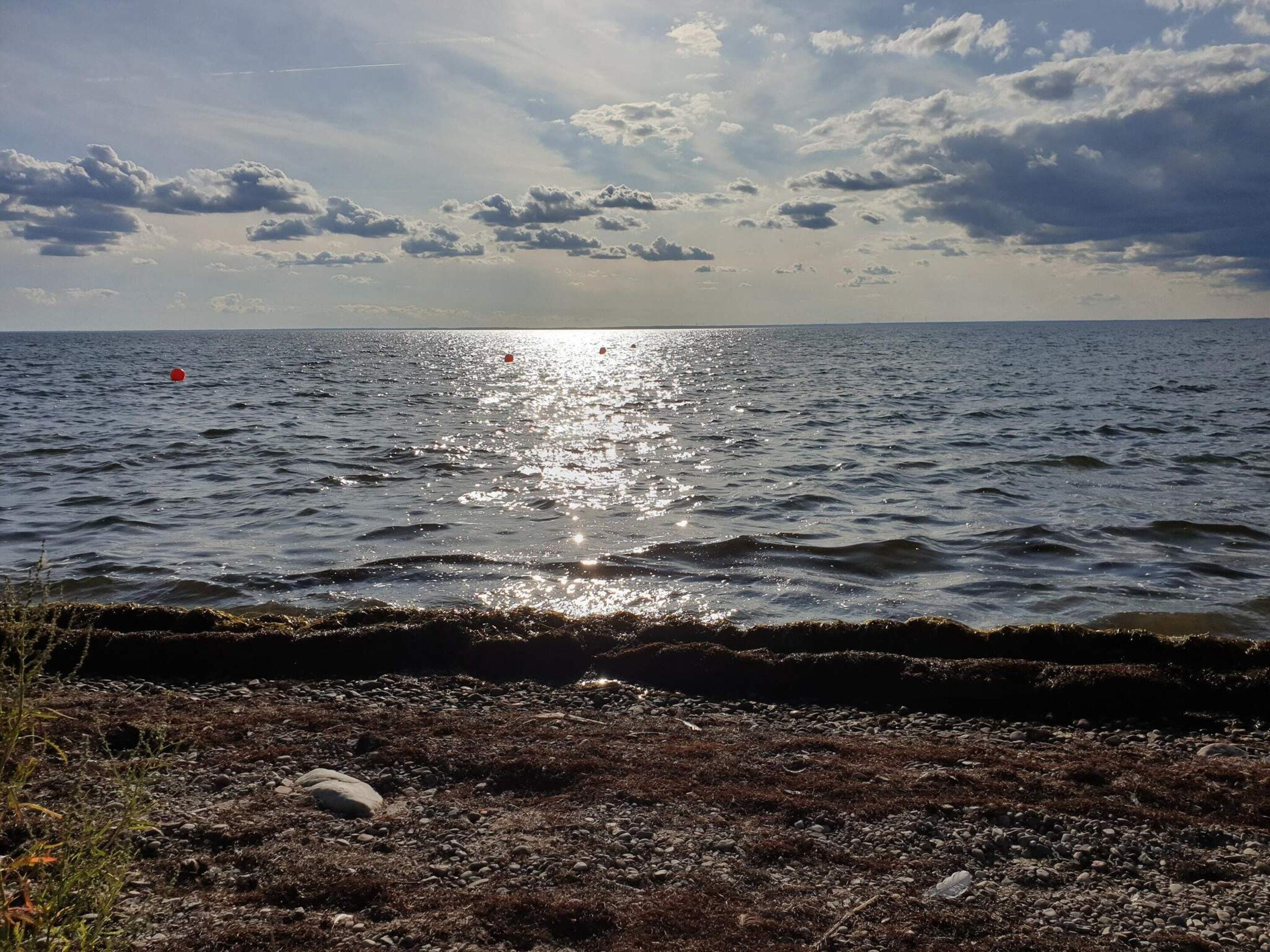 A coastal landscape with a rocky shoreline, calm sea, and a partly cloudy sky.