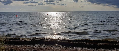 A coastal landscape with a rocky shoreline, calm sea, and a partly cloudy sky.