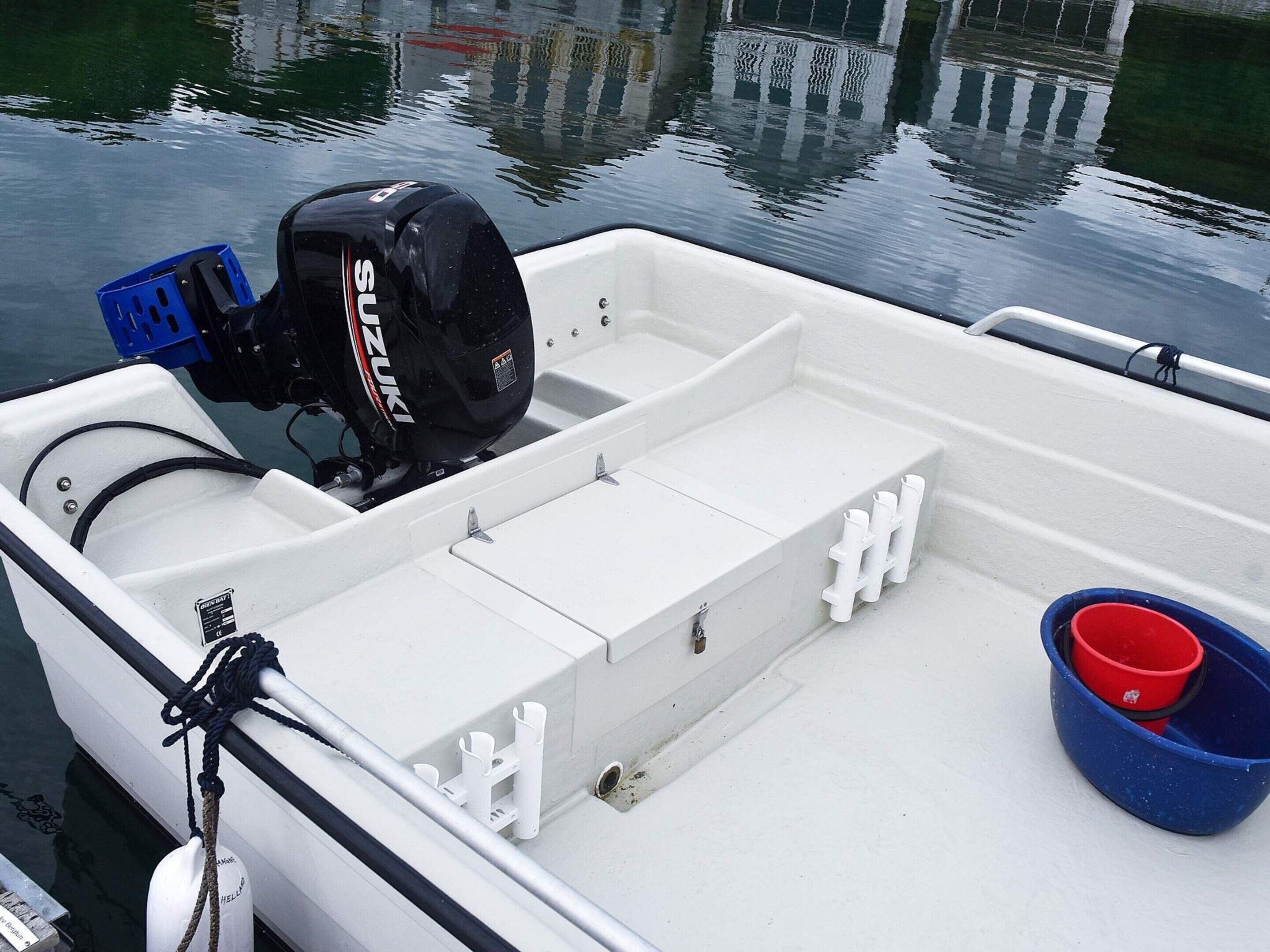 A small, white motorboat with a Suzuki outboard motor, a blue plastic basket, and a red bucket.