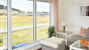 A living room with a large window, a white sofa, a glass coffee table with oranges, a small side table with a lamp, and a fluffy ottoman. - 8 Person Holiday Home in Leinoy-by Traum (Heroy)