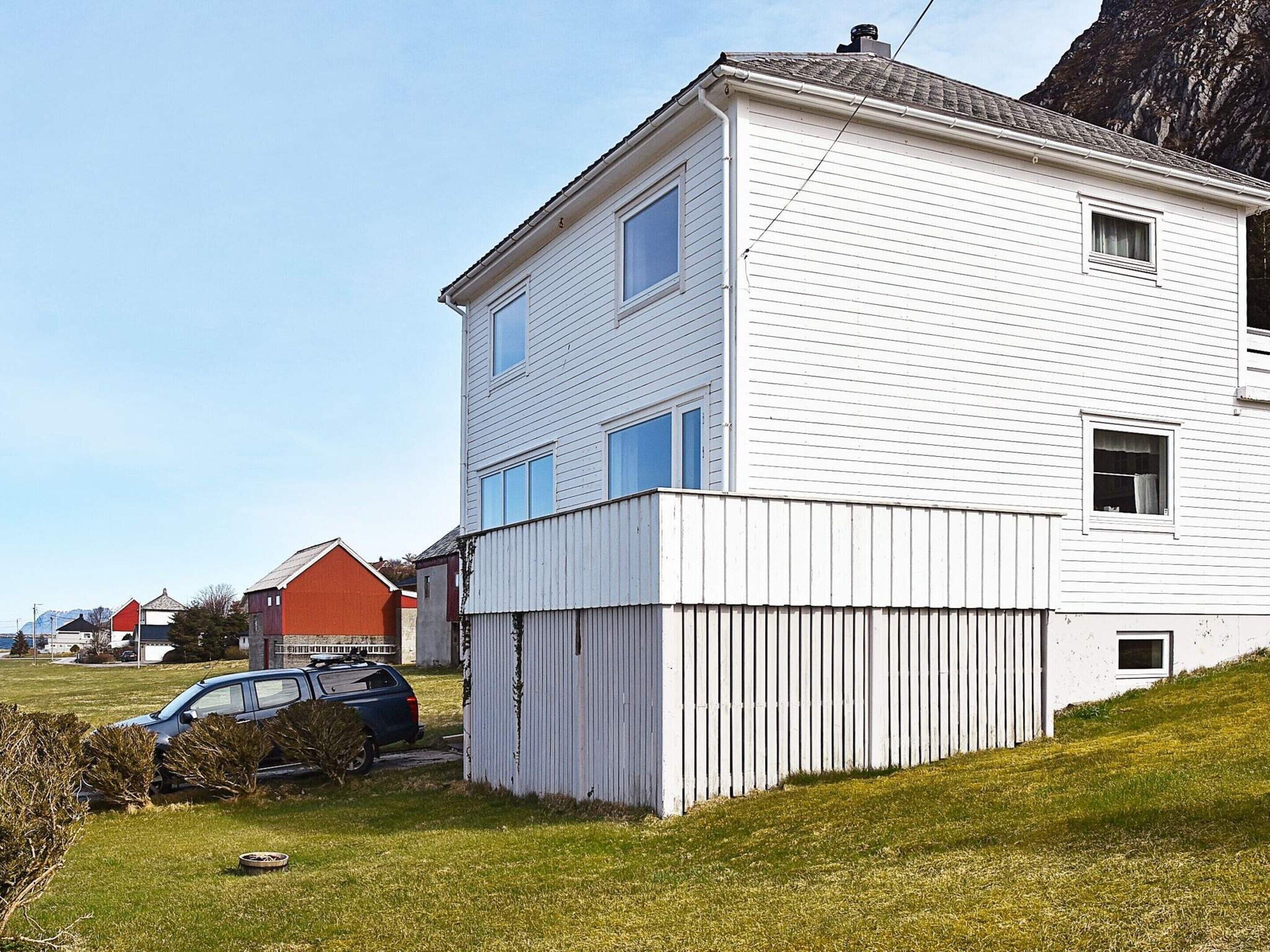 A white two-story house with a garage, a red barn, and a blue car parked in front.