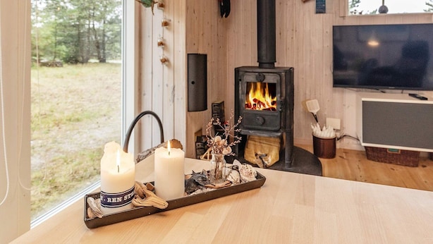 Ett mysigt rum med en vedeldad kamin, en tv och ljus placerade på ett brickbord.